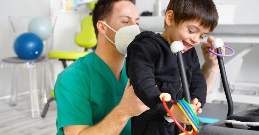 Child with cerebral palsy on physiotherapy in a children therapy center. Boy with disability doing exercises with physiotherapists in rehabitation centre. High quality photo.