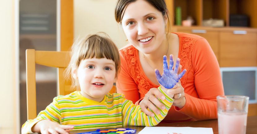 Happy mother and her child painting on paper with handprinting